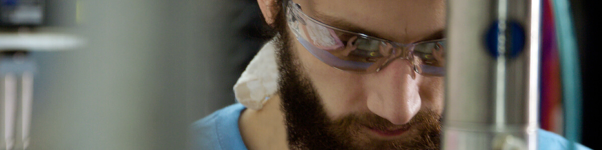 A man with safety glasses looks down while focusing on his work