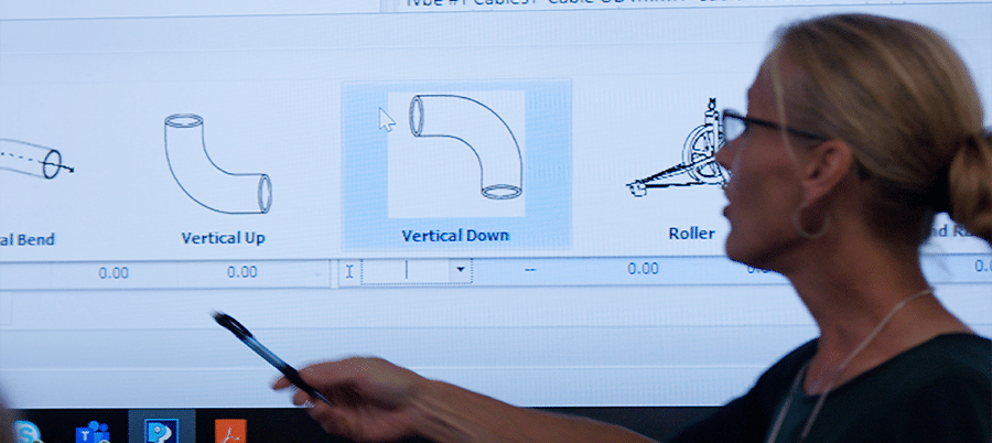 Una mujer rubia con anteojos, usa un bolígrafo para señalar una pantalla con una presentación del Pull-Planner de Polywater en ella.
