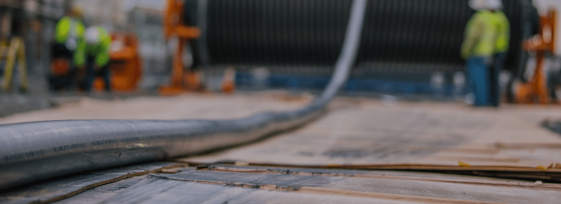 A long black high voltage electrical cable runs along the ground from the front left on a large cable reel that is blurred off in the distance on the right.