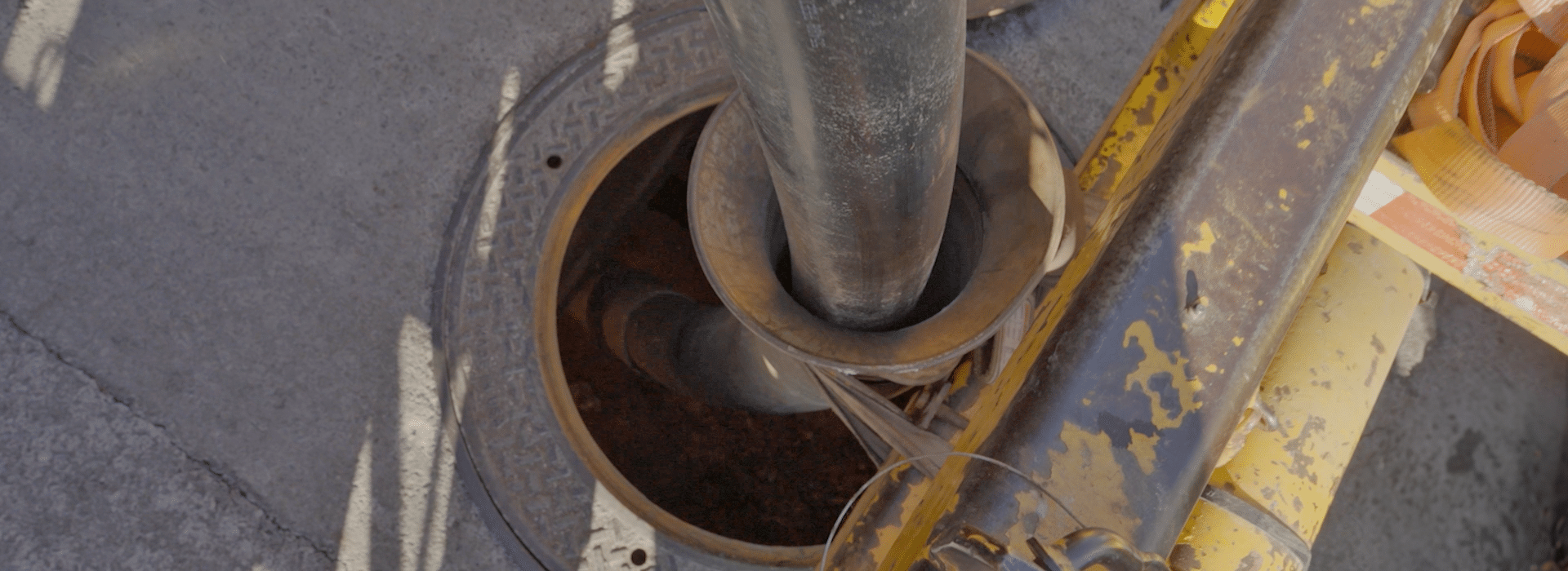 An overhead shot of a large black high-voltage cable entering an underground vault in a road.