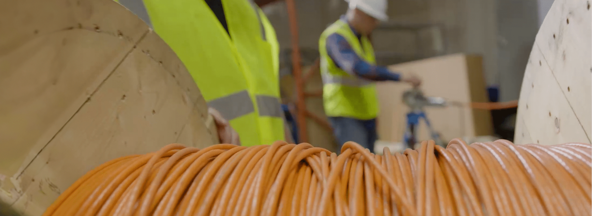 A close up of an spool of orange fiber optic cable. A blurry image of a man installing the fiber is in the background.