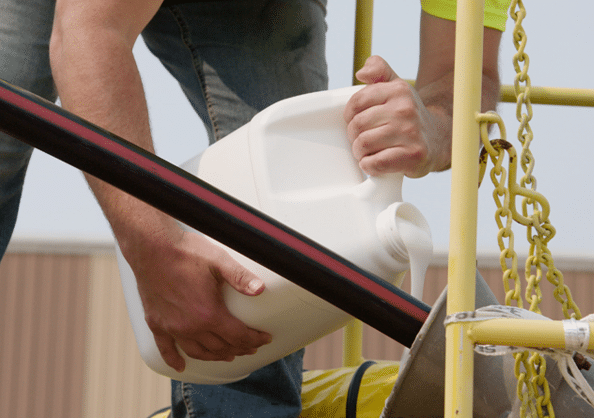 A person pouring a white Polywater lubricant from a white jug onto a electrical cable as it is pulled into a duct.