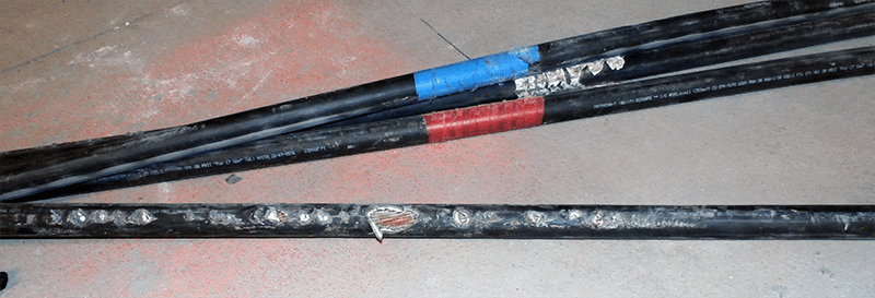 Three black electrical cables on the ground showing wear and tear. The bottom cable's sheath has burned through and is exposing electrical cable within.