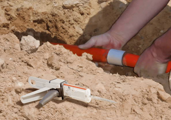 A man squeezing two sections of orange conduit together with a coupling that is adhered with Polywater BonDuit. A Polywater Bonduit cartridge in a dispensing gun lays on the ground in the foreground.