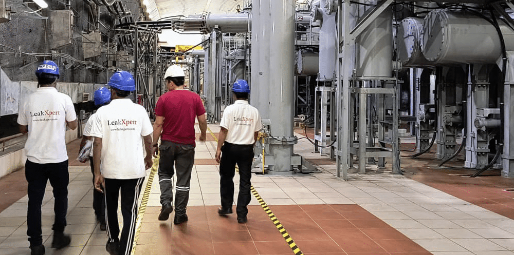 Five men in hard hats walking away from the camera as the tour an electrical transformer facility.